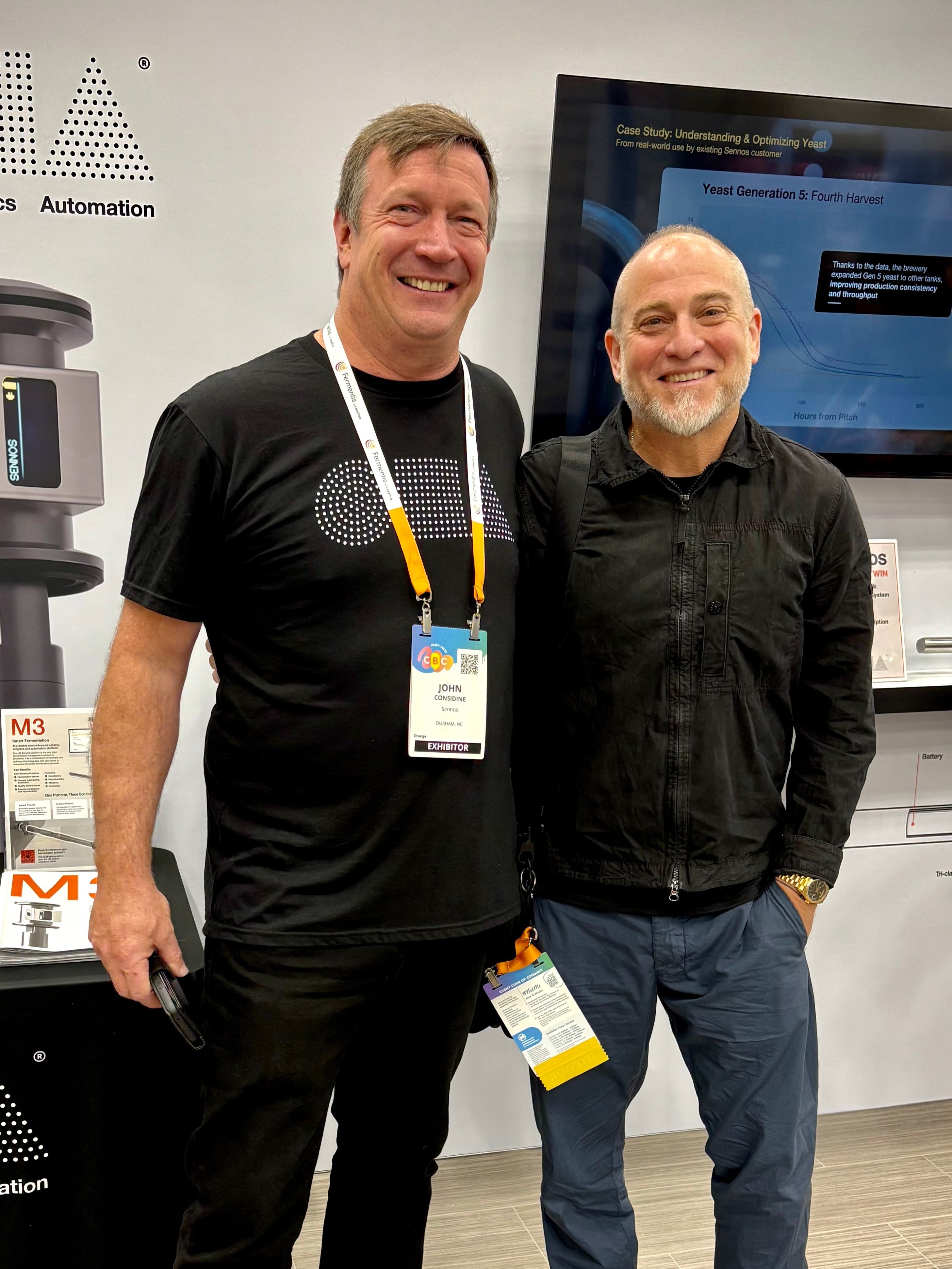 Two men standing in front of a booth with SGLIA branding at an event.