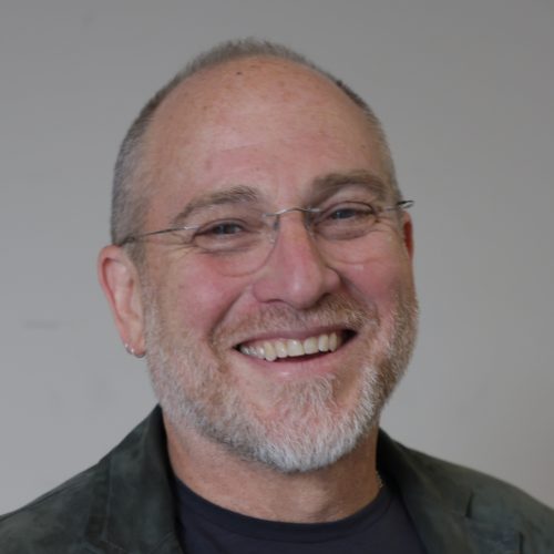 Man with glasses and a beard smiling against a plain background