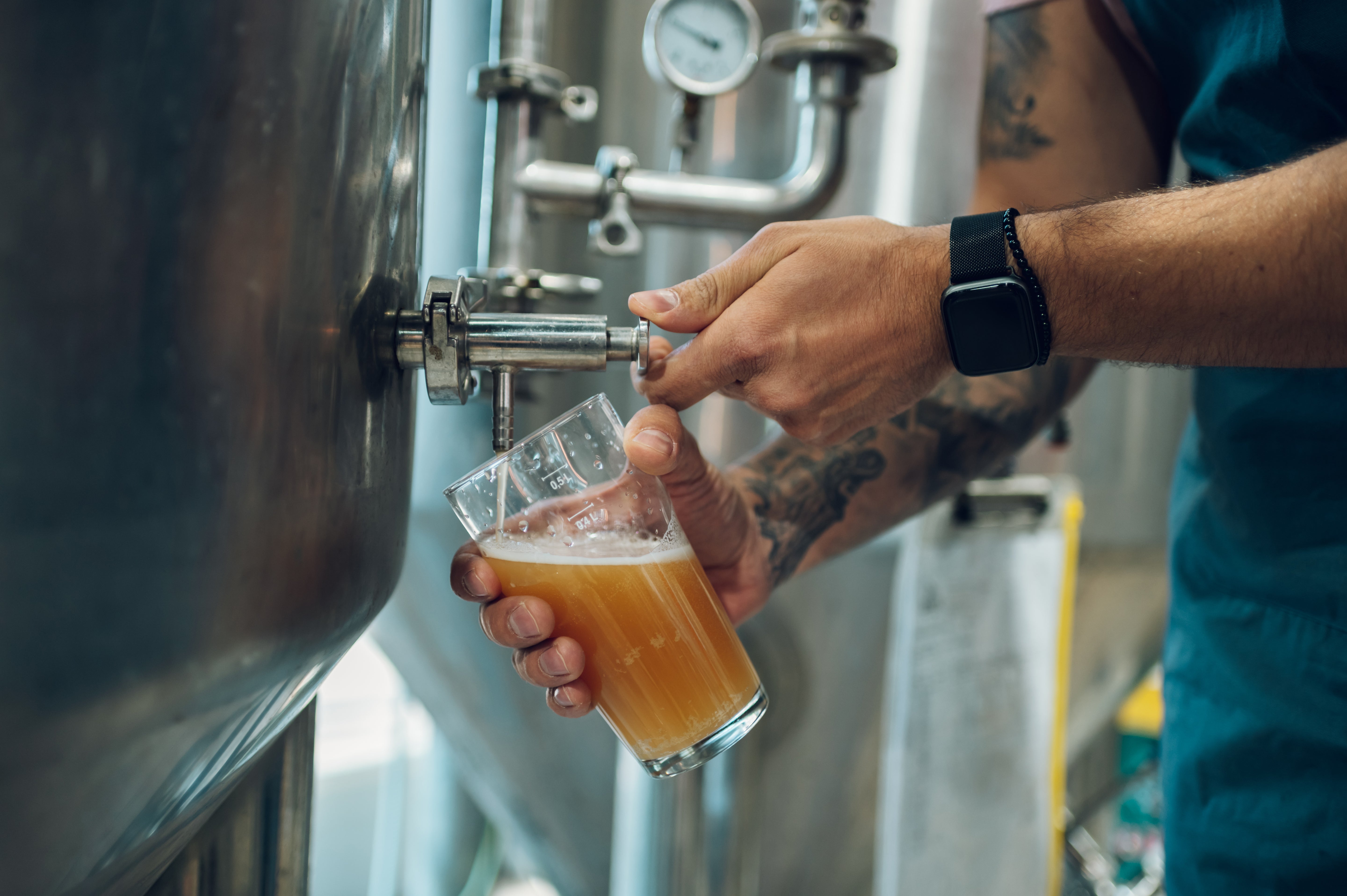 Person pouring beer from a tap into a glass in a brewery setting