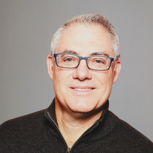 Man wearing glasses and a dark jacket against a gray background