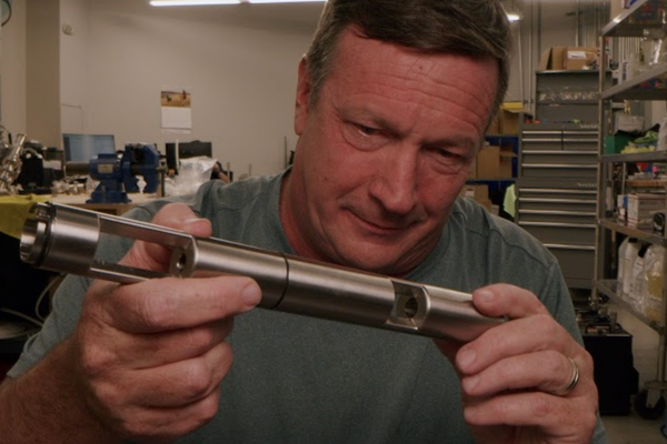 Man holding a metal cylindrical object in a workshop setting