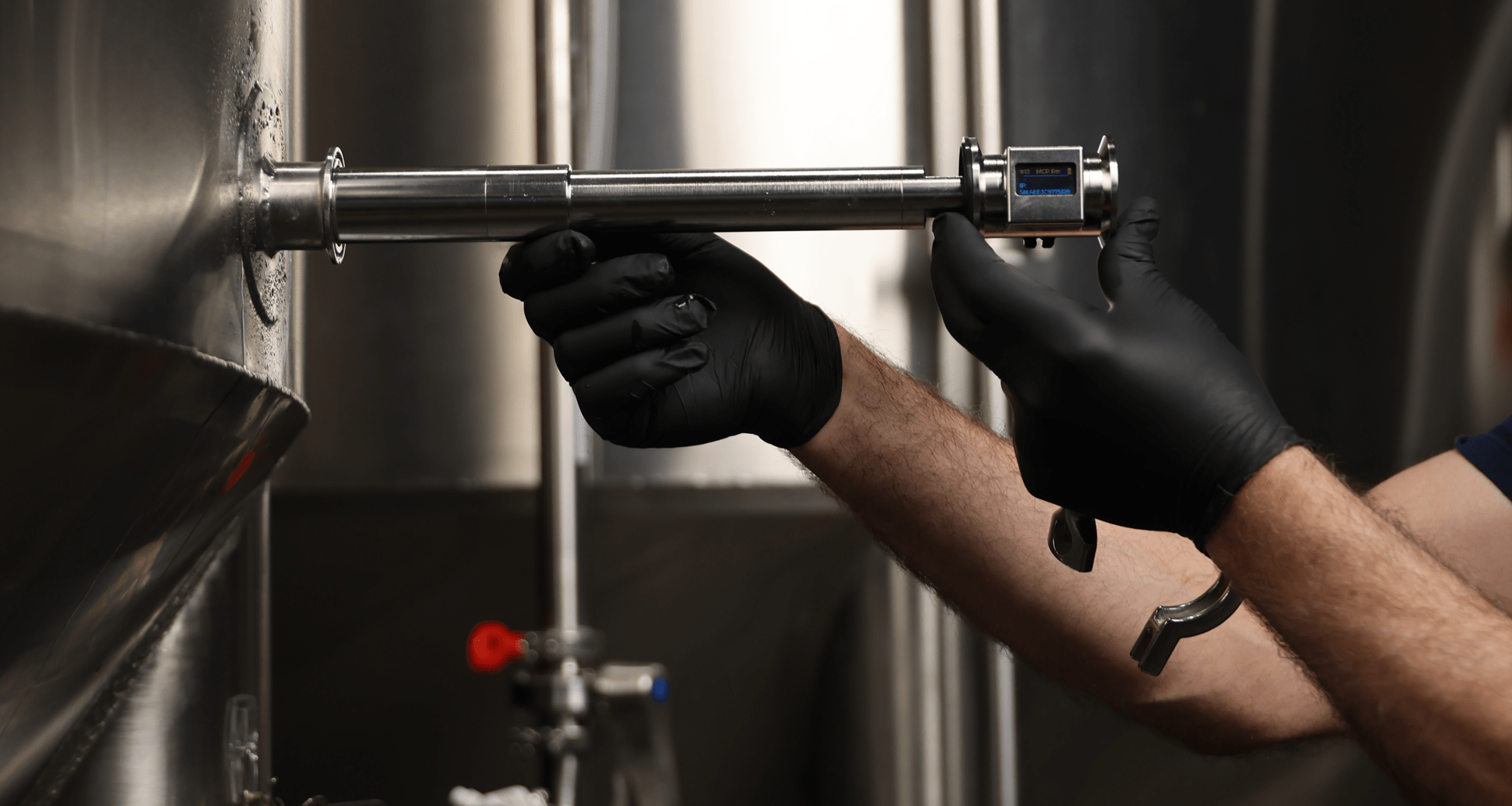 Person wearing black gloves using SennosM3 on a large metal tank, likely in a brewery setting.