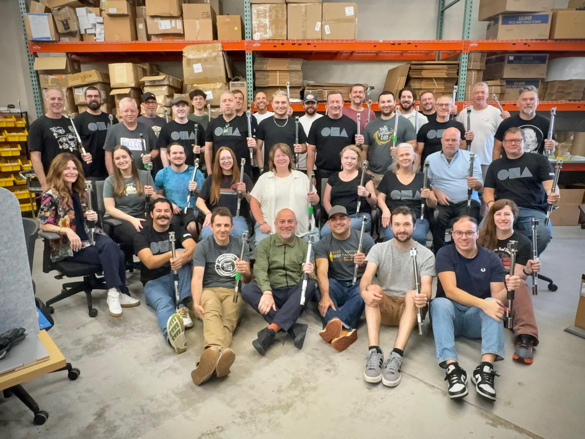 Group of people posing for a photo in a warehouse setting with boxes and equipment.