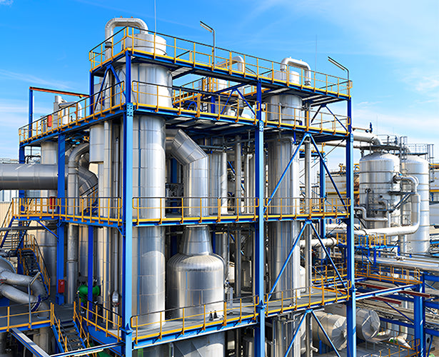 Industrial plant with large metal tanks and pipes against a blue sky.