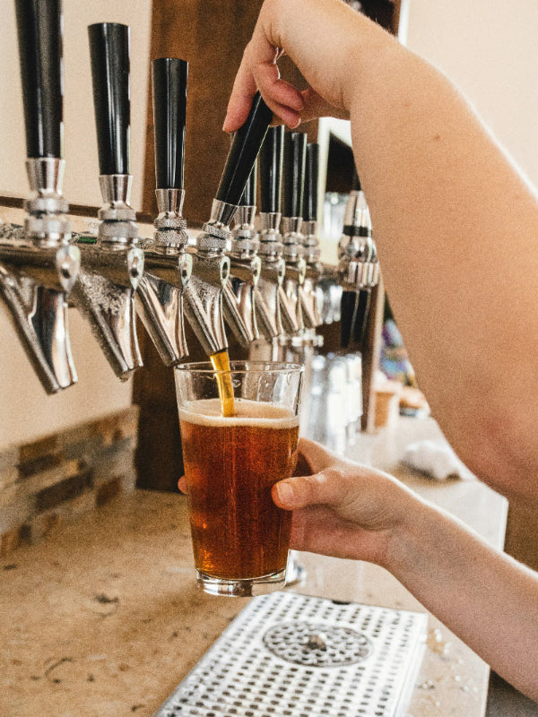 Person pouring beer from a tap into a glass at a bar.